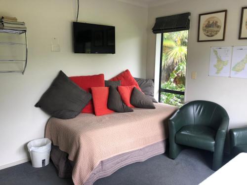 a bedroom with a bed with red pillows and a chair at Silverdale Garden Stay in Orewa