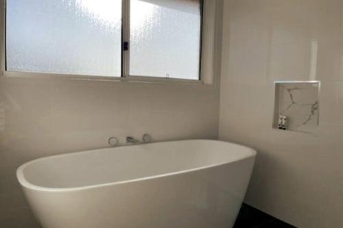 baño con bañera blanca y ventana en Cheerful 4-bedroom family retreat in Caves Beach, en Caves Beach
