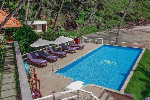 a swimming pool with chairs and umbrellas next to it at Rockholm at the Light House Beach in Kovalam