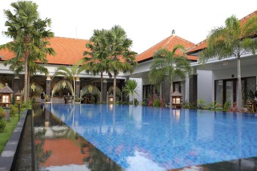 a swimming pool in front of a building with palm trees at Kubu Garden Suites & Villas Nusa Dua in Nusa Dua