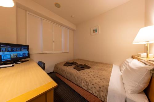 a hotel room with a bed and a desk with a television at Sanco Inn Toyota in Toyota