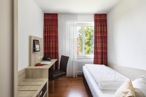 une chambre d'hôtel avec un lit, un bureau et une fenêtre dans l'établissement Caritas Tagungszentrum, à Fribourg-en-Brisgau