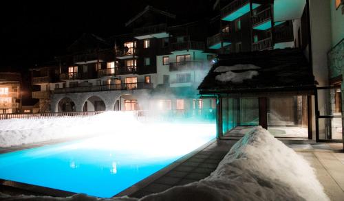 - une piscine avec de la neige et des bâtiments la nuit dans l'établissement Les Alpages De Val Cenis, à Lanslebourg-Mont-Cenis