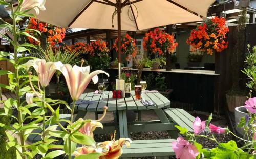 a picnic table in a garden with flowers and an umbrella at Sibton White Horse Inn in Saxmundham
