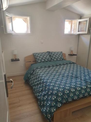 a bedroom with a bed with a blue comforter and two windows at un air de vacances in Laroque-des-Albères