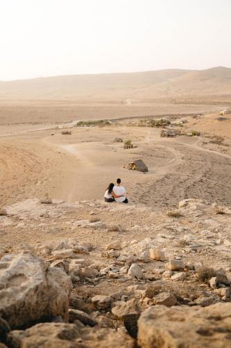 a couple sitting on the rocks in the desert at Succah in the Desert in Mitzpe Ramon