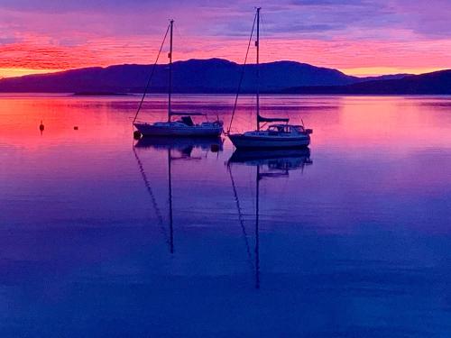 two boats sitting in the water at sunset at Creran Apartment, Kinlochlaich House in Appin
