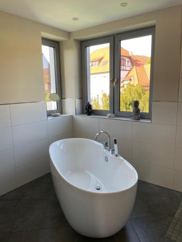 eine weiße Badewanne im Bad mit zwei Fenstern in der Unterkunft Ferienwohnung Werratal in Obermaßfeld-Grimmenthal