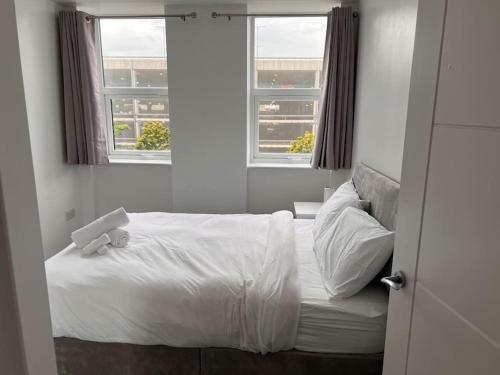 a bedroom with a bed with white sheets and two windows at 2 Bed Apt, 20 mins from London, central romford in London