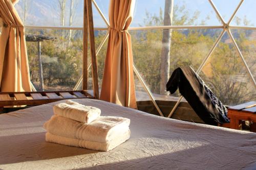 a pile of towels on a bed with a large window at Domos Uspallata in Uspallata