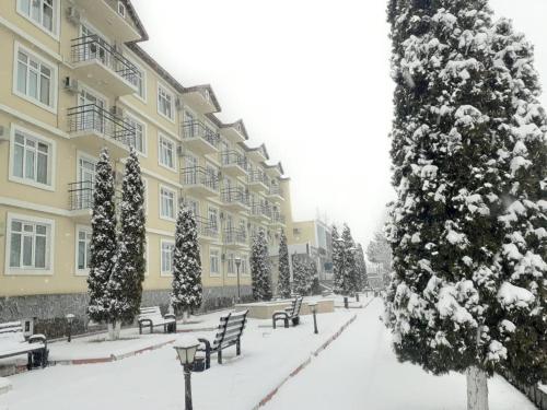 un patio cubierto de nieve de un edificio con árboles y bancos en Gabala Hotel en Daşca