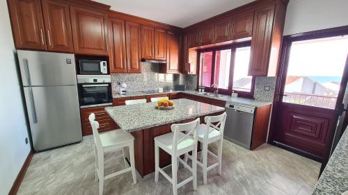 a kitchen with wooden cabinets and a kitchen island with white chairs at Santa Luzia Apt 59 A in Ribeira Grande