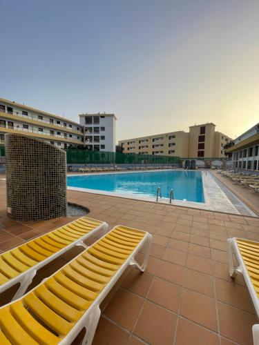 a swimming pool with two yellow benches in a building at Apartament Modern 1 Playa del Ingles in San Bartolomé de Tirajana