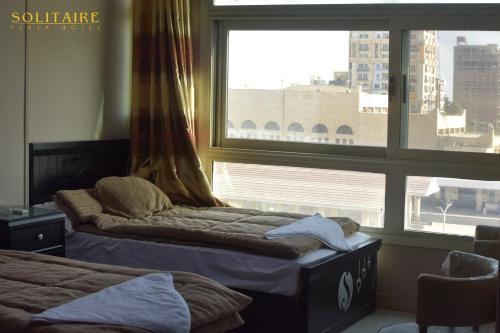 two beds in a room with a large window at Solitaire Plaza Hotel-Ismailia Train Station in Ismailia