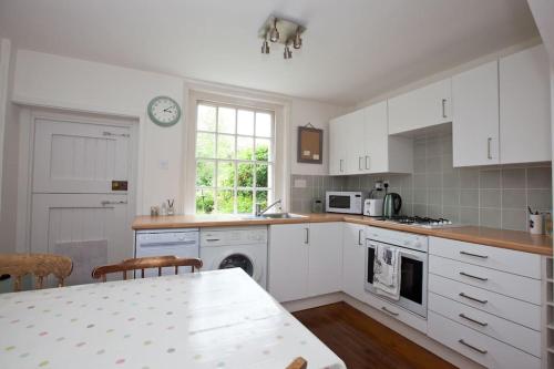 a kitchen with white cabinets and a table and a clock at Quaker Cottage in historic Arundel in Arundel