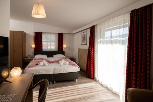 a bedroom with a bed with red curtains and a table at Parkhotel Zur Linde in Silandro