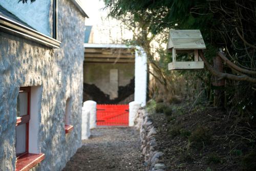 a building with a red gate and a house at Cobblers Cottage Creggan in Greencastle