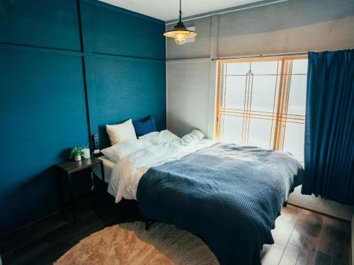 a blue bedroom with a bed and a window at ゲストハウスVACILANDO in Chitose