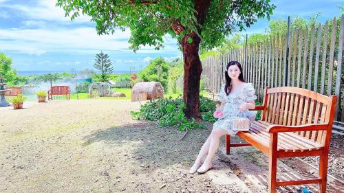 a woman sitting on a bench under a tree at 墾丁勿忘我城堡莊園 in Hengchun