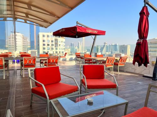 a patio with red chairs and tables and an umbrella at Swiss-Belhotel Seef Bahrain in Manama