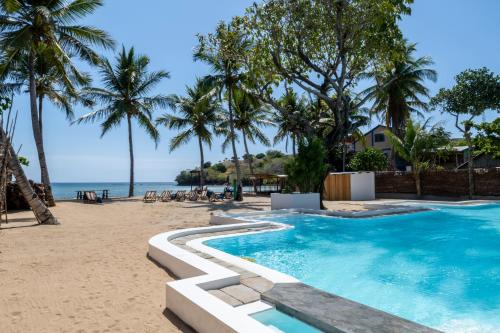 una piscina junto a una playa con palmeras en Swisscocobeach, en Nosy Be