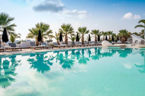 a swimming pool with chairs and palm trees at Smy Mediterranean White Santorini in Kamari