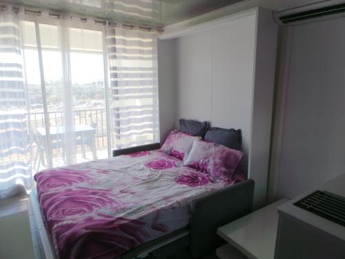 - une chambre avec un lit avec des draps roses et une fenêtre dans l'établissement le select Héliopolis hg, au Cap d'Agde