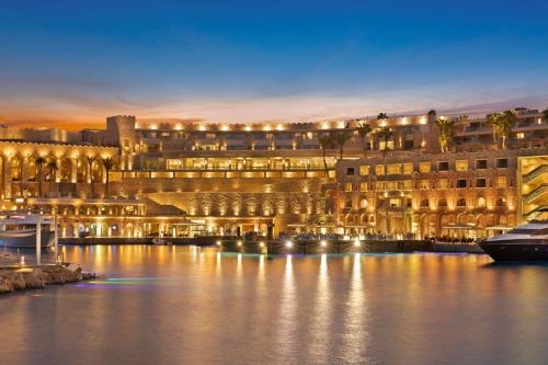 Pickalbatros Citadel Resort Sahl Hasheesh في الغردقة: مبنى كبير به اضاءة على الماء ليلا