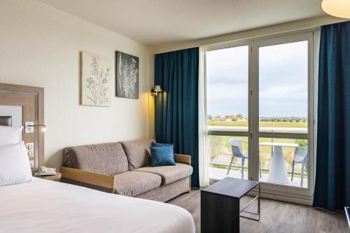 a hotel room with a bed and a couch and a window at Novotel Senart Golf De Greenparc in Saint-Pierre-du-Perray