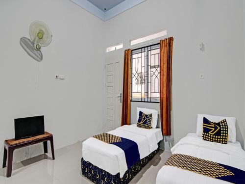 a room with two beds and a tv and a window at OYO 91847 Rumah Singgah Kinaya Syariah in Parit