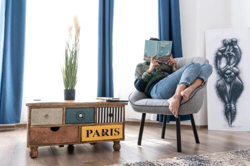 a woman sitting in a chair reading a book at Zakarias Apartments in Miercurea-Ciuc