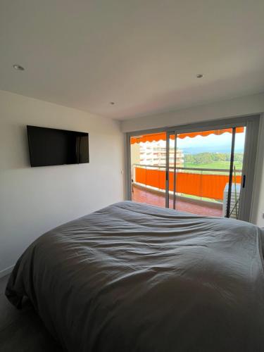 Schlafzimmer mit einem Bett, einem TV und einem Balkon in der Unterkunft Appartement 2 pièces vue mer, à proximité de tout in Mandelieu-la-Napoule