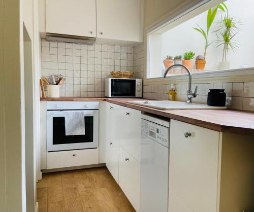 eine Küche mit weißen Schränken, einem Waschbecken und einem Fenster in der Unterkunft GÎTE DE LA MUSARDE in Villers-sur-Mer