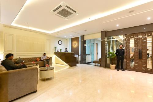 a man standing in a lobby with people sitting on couches at Hotel Avalon Palms Agra in Agra