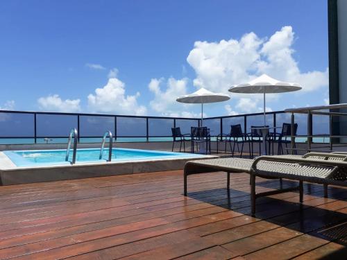 a balcony with a swimming pool and tables and umbrellas at Flat pé na areia Tambaú in João Pessoa