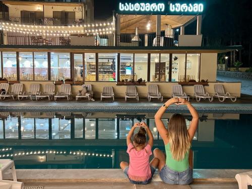 two girls sitting on the edge of a swimming pool at Hotel Surami in Surami