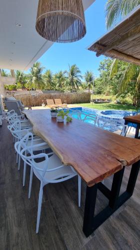 a wooden table with white chairs and a pool at Vila Leão do Norte in Japaratinga