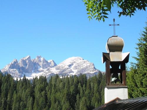 a church steeple with a cross and a mountain at Hotel Garnì Miramonti in Falcade