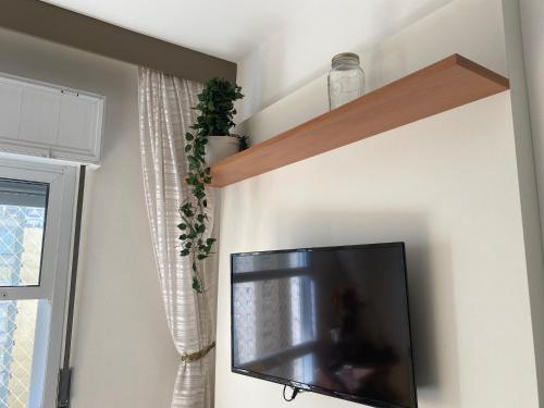 Une télévision à écran plat est installée sur un mur à côté d'une fenêtre. dans l'établissement Guaruja Pitangueiras apto na praia, à Guarujá