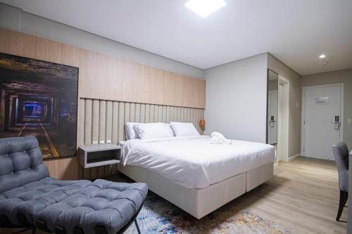 a bedroom with a large white bed and a chair at Hotel Darolt Criciúma in Criciúma