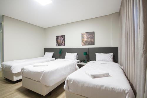 a hotel room with three beds with white sheets at Hotel Darolt Criciúma in Criciúma