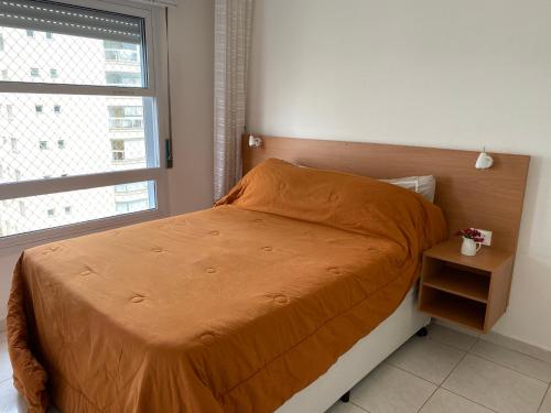 une chambre avec un lit avec une couette orange et une fenêtre dans l'établissement Guaruja Pitangueiras apto na praia, à Guarujá