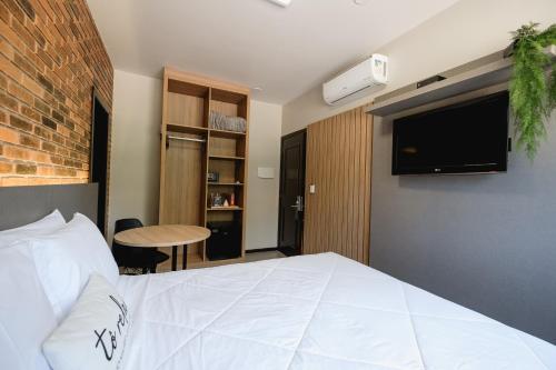 um quarto com uma grande cama branca e uma televisão em Malbec Casa Hotel em Bento Gonçalves