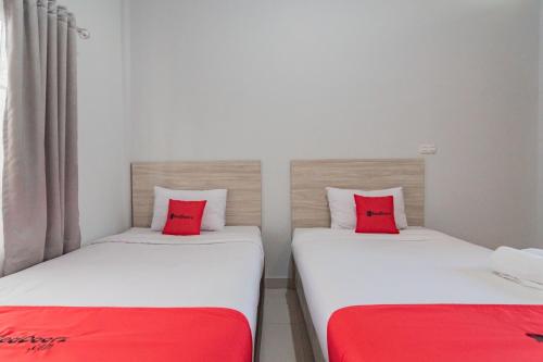 two beds with red pillows in a room at RedDoorz Plus Syariah @ Tuparev Cirebon 3 in Cirebon