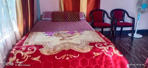 um quarto com uma cama com uma colcha vermelha e 2 cadeiras em Relax Home em Mawlynnong