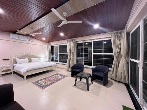 a bedroom with a bed and chairs and windows at The Riverside Estate - 2Bedroom Private Pool Villa in Udaipur in Udaipur