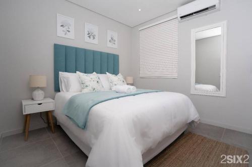 Schlafzimmer mit einem großen weißen Bett mit blauem Kopfteil in der Unterkunft Unit 700 @2SIX2 on Florida in Durban