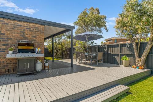 una terraza de madera con parrilla y sombrilla en Dromana Beach Holiday House *3 minutes to the sand, en Safety Beach