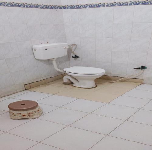 a bathroom with a toilet in a white tiled room at Jiya Green Garden & Banquet, Sonipat in Sonīpat