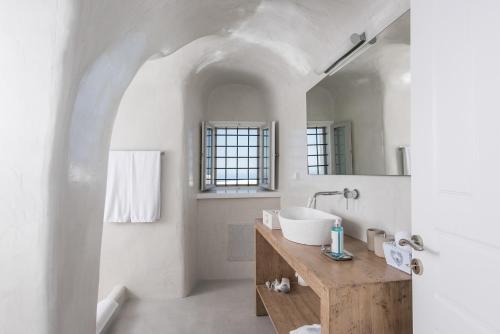 a white bathroom with a sink and a mirror at Aqua Luxury Suites by NOMÉE Hospitality Group in Imerovigli